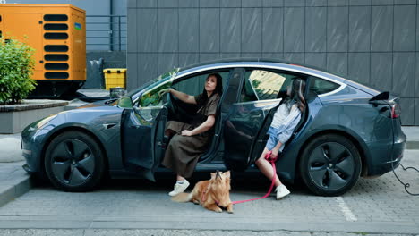 mujeres y un perro cerca de un coche eléctrico cargando