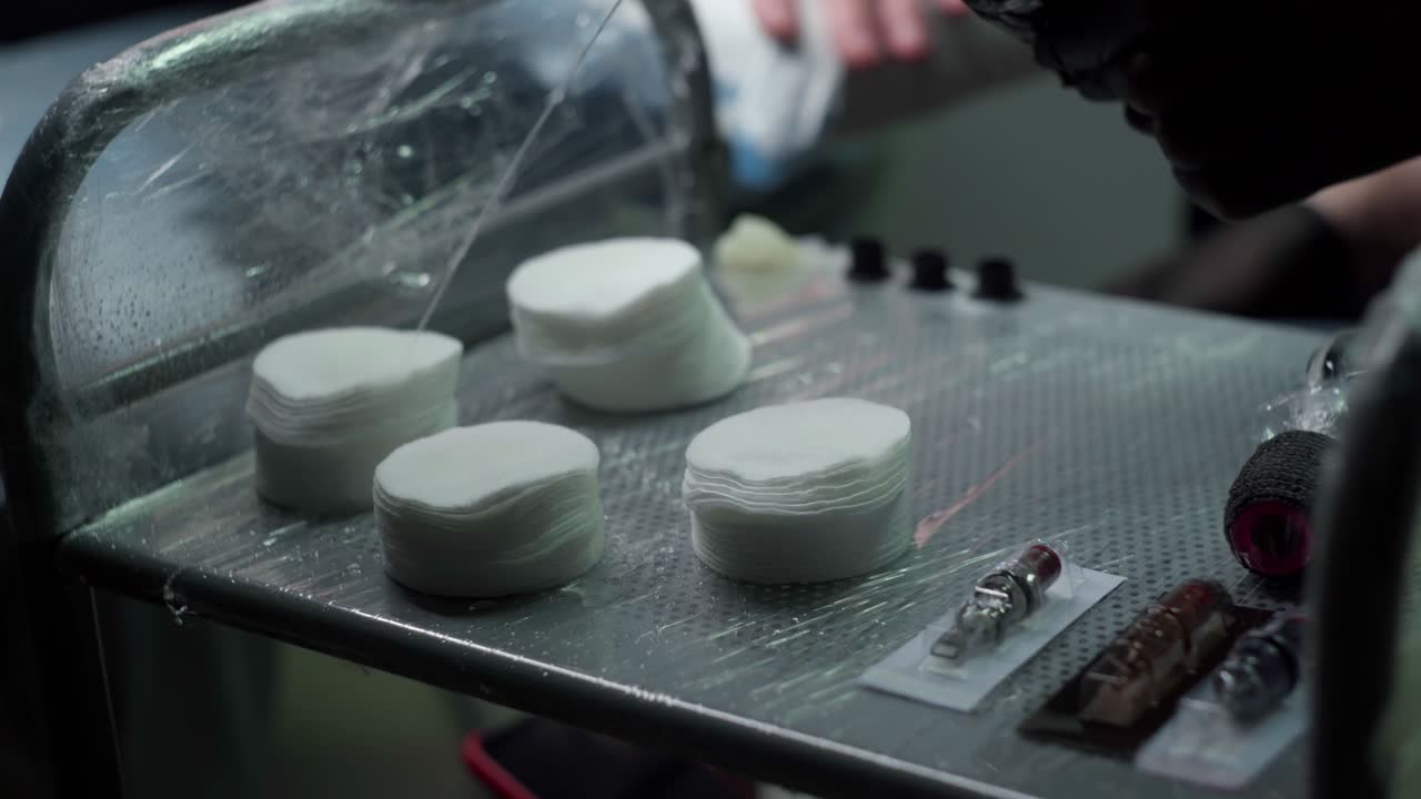 익명의 문신사가 문신실에서 테이블 위에 물로 목화 패드를  ⁇ 고 있습니다.