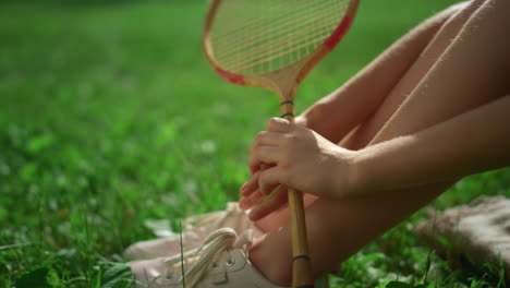 closeup girl legs hand holding badminton racket in park. kid sit blanket alone