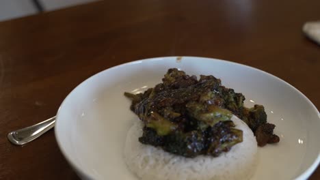 a steaming hot plate of broccoli and beef stir fry on a bed of sticky rice