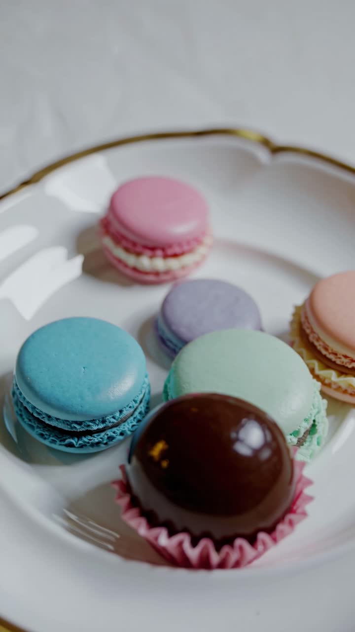 Close-up video shot of colorful macarons and a chocolate dessert on a white plate