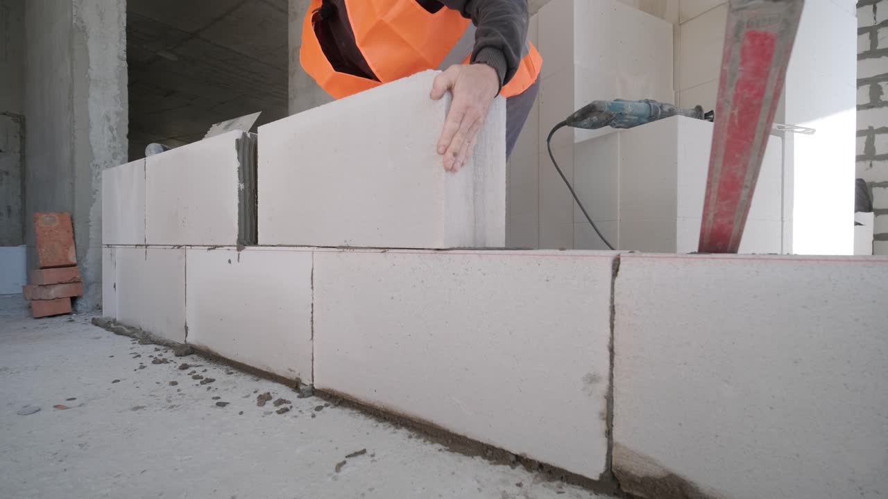 벽돌공은 오토클레이브 된 공기 콘크리트 블록에 접착용 접착제를 적용합니다. 벽돌 작업자 계약자는 레이저 레벨로 벽돌을 만드는 폼 콘크리트에서 과도한 모터를 제거합니다.