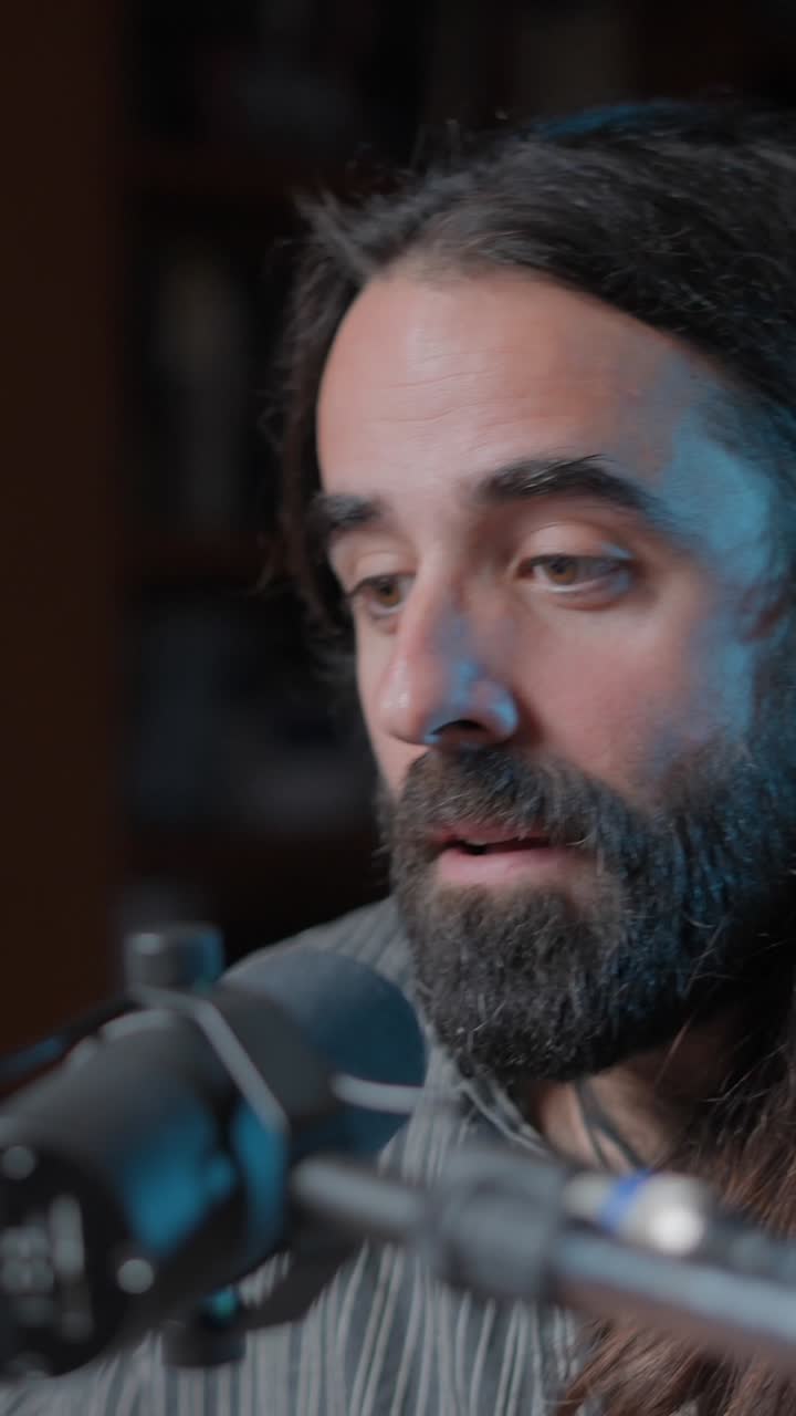 Close-up of a man with long hair and a beard speaking into a microphone ...