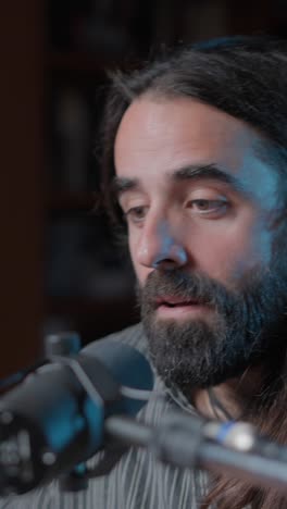close-up of a man with long hair and a beard speaking into a microphone