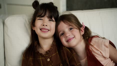 Happy-funny-girl-foster-sisters-hugging-and-laughing-on-sofa