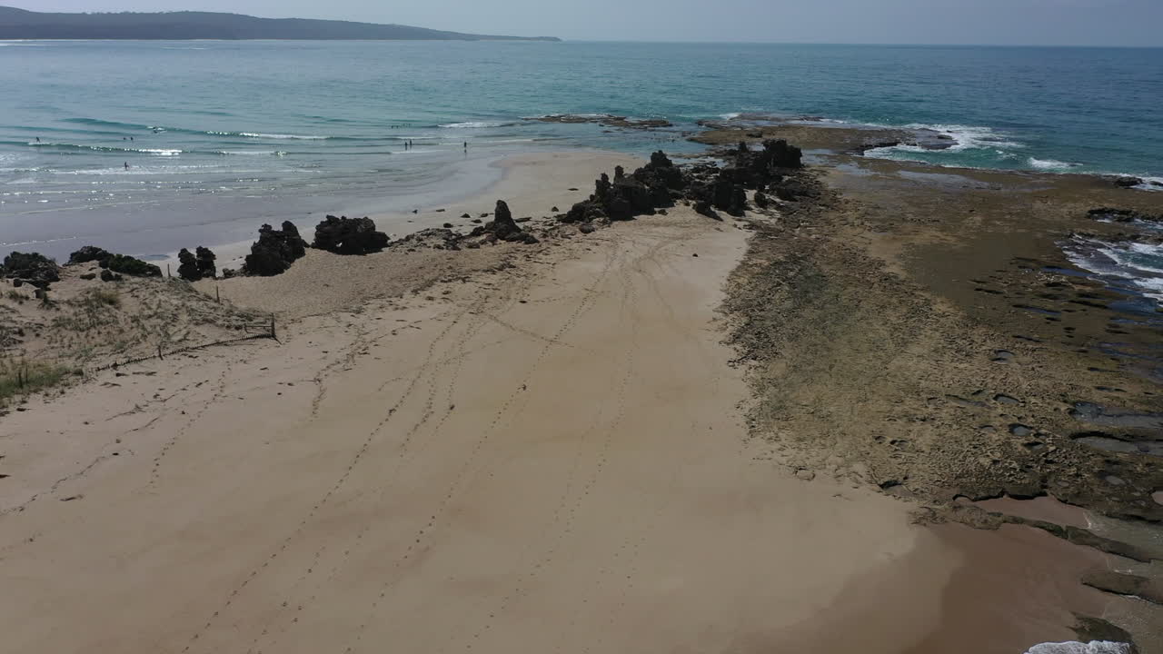 햇볕이 잘 드는 모래 바다 해변 위의 바위가 많은 태평양 도로로 공중 하강
