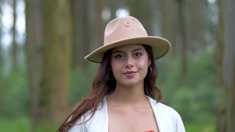 Beauty-of-an-Ecuadorian-woman-in-a-hat-and-white-top-with-open-hair,-as-she-finds-tranquility-in-the-forest,-closing-her-eyes-before-slowly-opening-them-with-a-radiant-smile