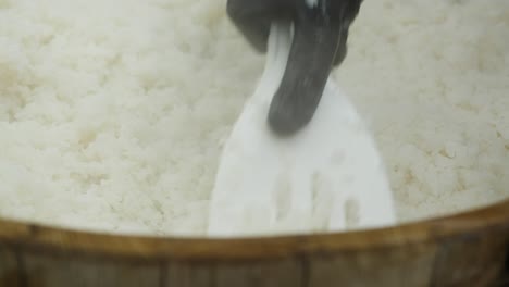 cook stirs hot rice in a wooden bowl