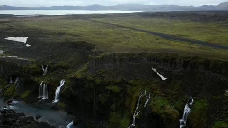 Aerial-view-from-Sigöldugljúfur-canyons-in-Iceland-with-waterfalls-with-aqua-blue-water-of-Tungnaá-River-and-abundant-green-vegetation-and-empty-black-roads,-surrounded-by-rivers-and-mountains