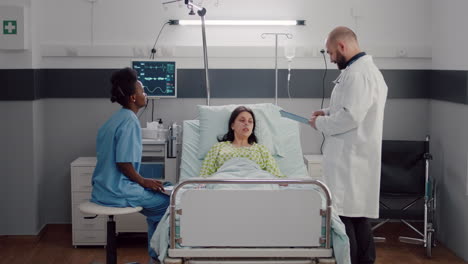 Front-view-of-sick-woman-lying-on-bed-while-afro-american-nurse-analyzing-x-ray-bones