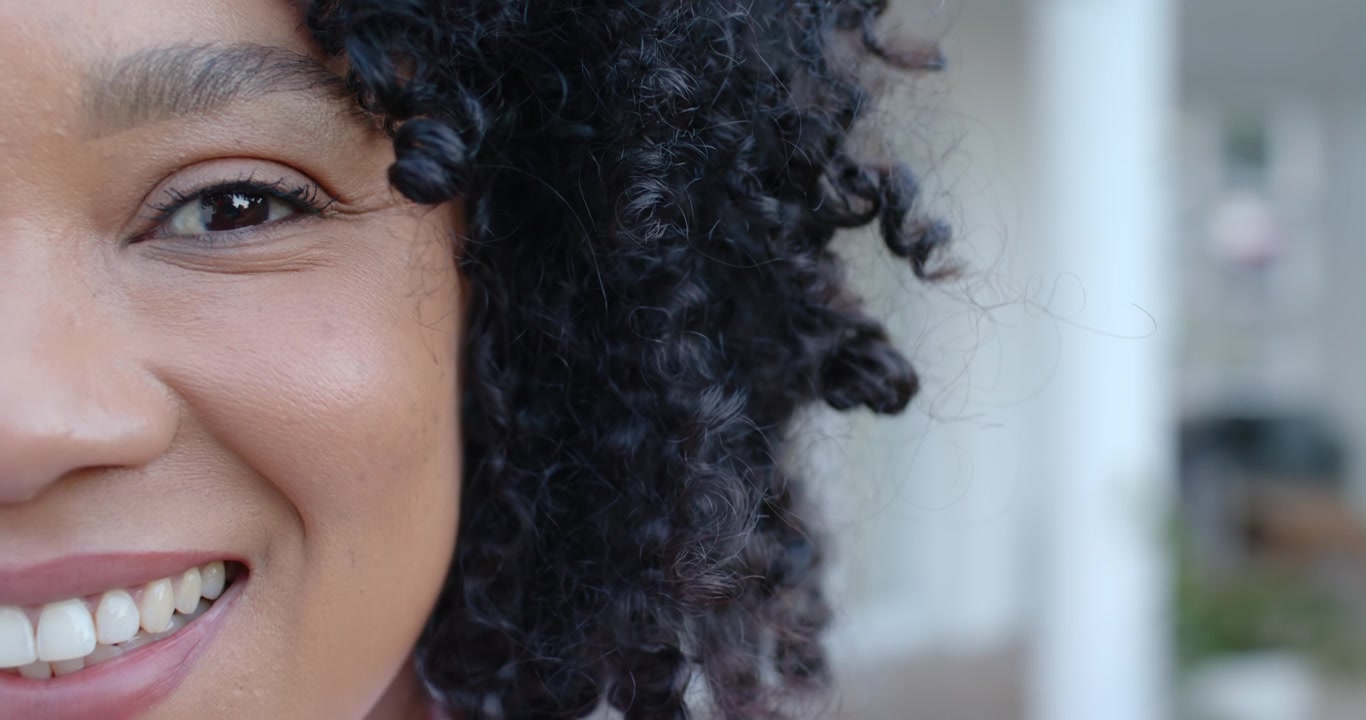 Donna afroamericana che riceve un segnale dalla telecamera, guarda, batte le palpebre, trasformandosi in un ampio sorriso sul portico