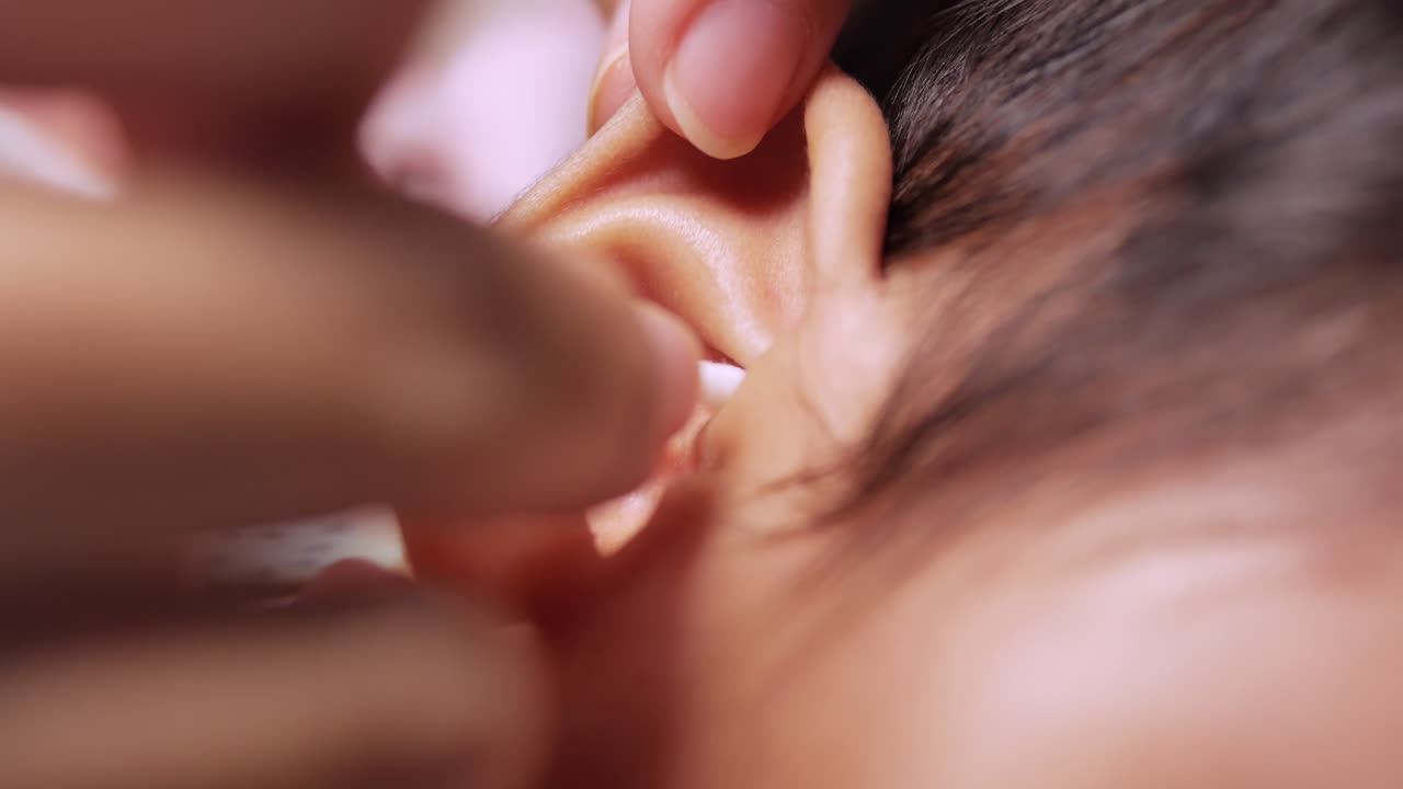 A nurturing moment as a caregiver gently cleans a baby girl's ear with care and tenderness.