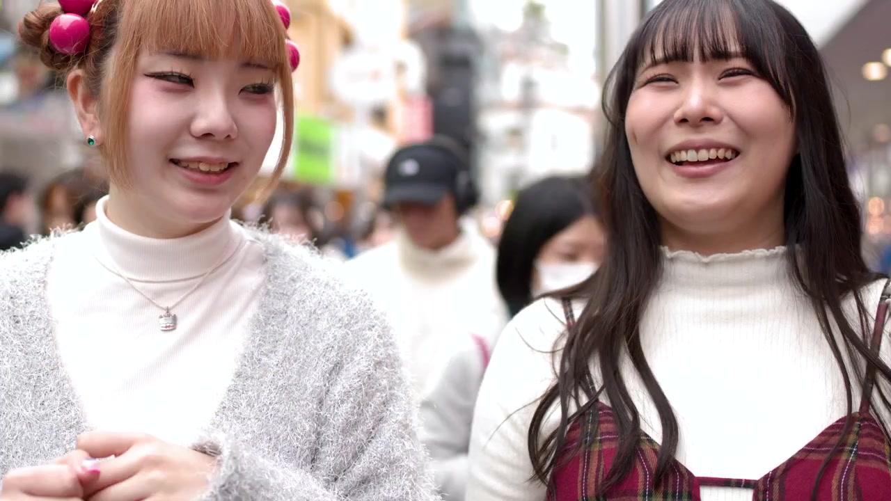 混雑した通りを歩きながら話したり指差したりしている、おしゃれな若い女性2人のクローズアップ。