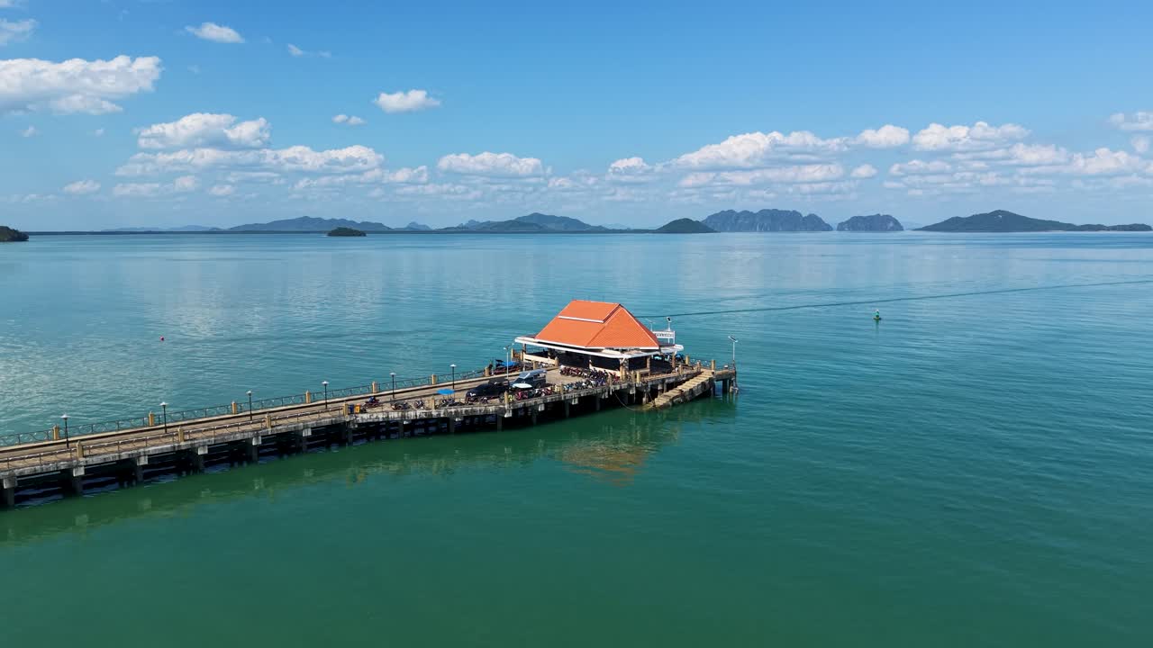 Cảnh quay cận cảnh bằng drone Bến tàu Cổ trấn Koh Lanta ở Thái Lan, với một chiếc xe tay ga chạy dọc bến tàu, đại dương màu xanh ngọc lam và những hòn đảo nhiệt đới xa xa dưới bầu trời xanh rực rỡ.