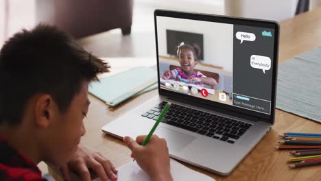 Schoolboy-using-laptop-for-online-lesson-at-home,-with-school-friend-and-web-chat-on-screen