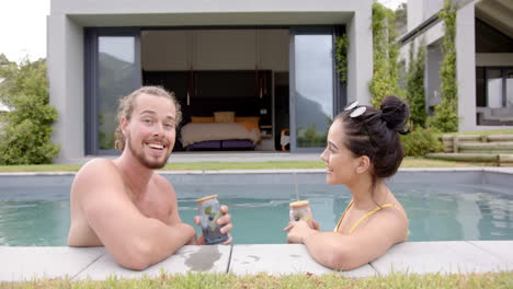 a young biracial couple relaxes by pool with drinks