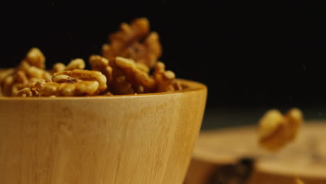 close up shot of walnuts dropping into wooden bowl against black studio background shot in slow motion