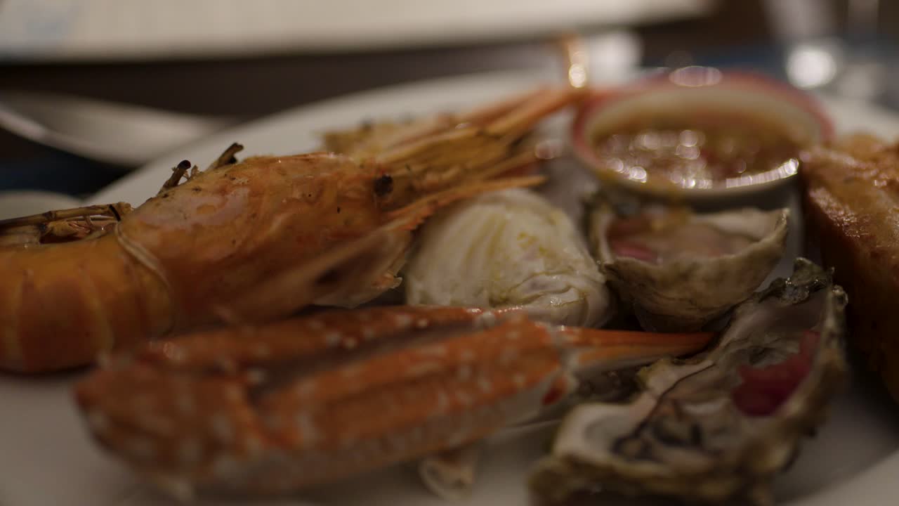 Plate of shrimp, oyster, crab, and sauce in warm, low-light restaurant, camera slowly focuses