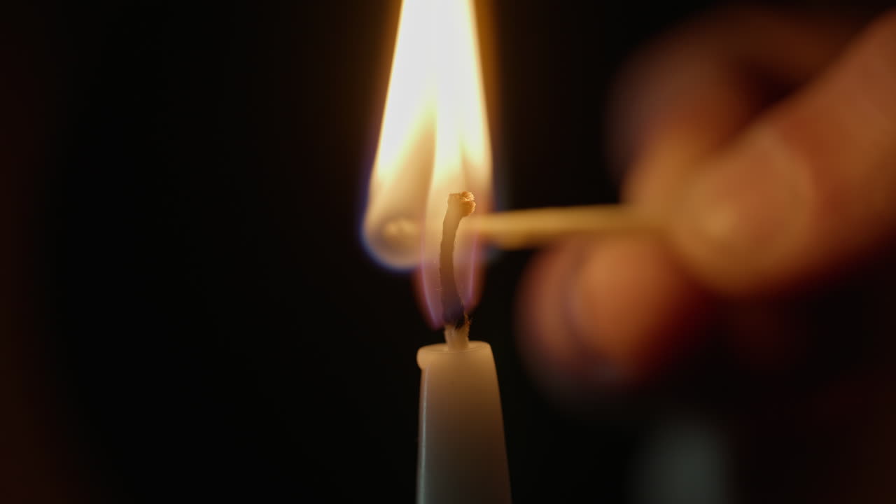 Hand grips wooden match striking paraffin candle on dark room backdrop closeup