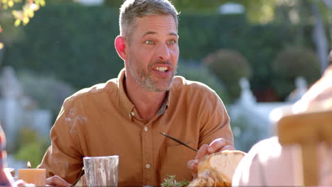 happy diverse male and female friends eating thanksgiving celebration meal in sunny garden