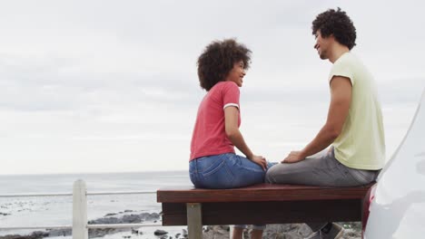 african american couple smiling while talking to each other sitting on a bench on the promenade