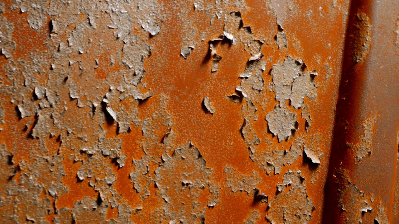 Nærbillede af rusten, afskallende maling på metal, afskallende orangebrun overflade på et forladt fabrikspanel med tekstur.