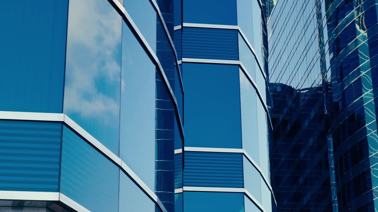 Arquitectura empresarial moderna con paredes de cristal y acero que reflejan nubes en el cielo.