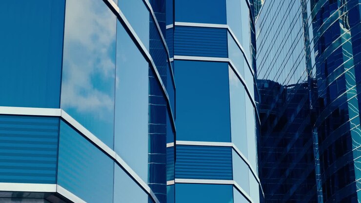 Architettura aziendale moderna con pareti di vetro e acciaio che riflettono le nuvole del cielo.