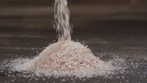 slow motion, coarse sea salt being poured and piled on concrete ground