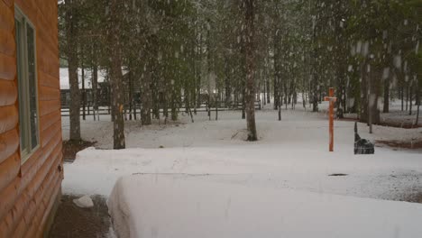 a thick snowfall at the view of a side of a cabin with some thick snow on the ground