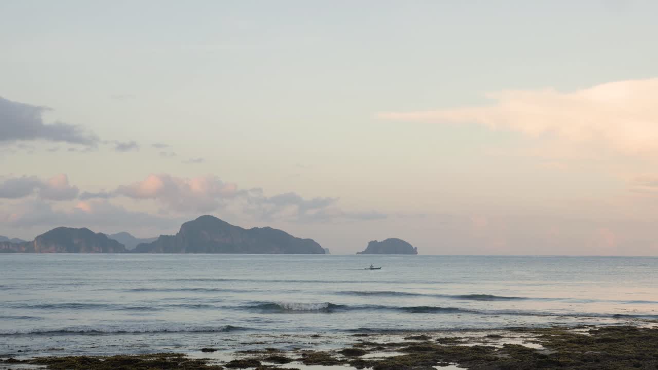 황혼 때 석회암 절벽 앞에서 멀리 보트를 타고 노를 젓는 남자