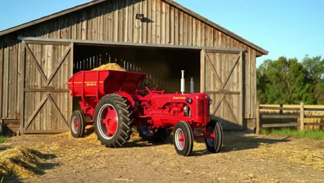 a vibrant red tractor is seen exiting a rustic barn while unloading hay, embodying the essence of agricultural life and the charm of rural farming in sunny weather