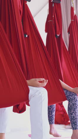 women sit in comfortable fly yoga hammocks meditating in butterfly poses with fingers in mudra position closeup