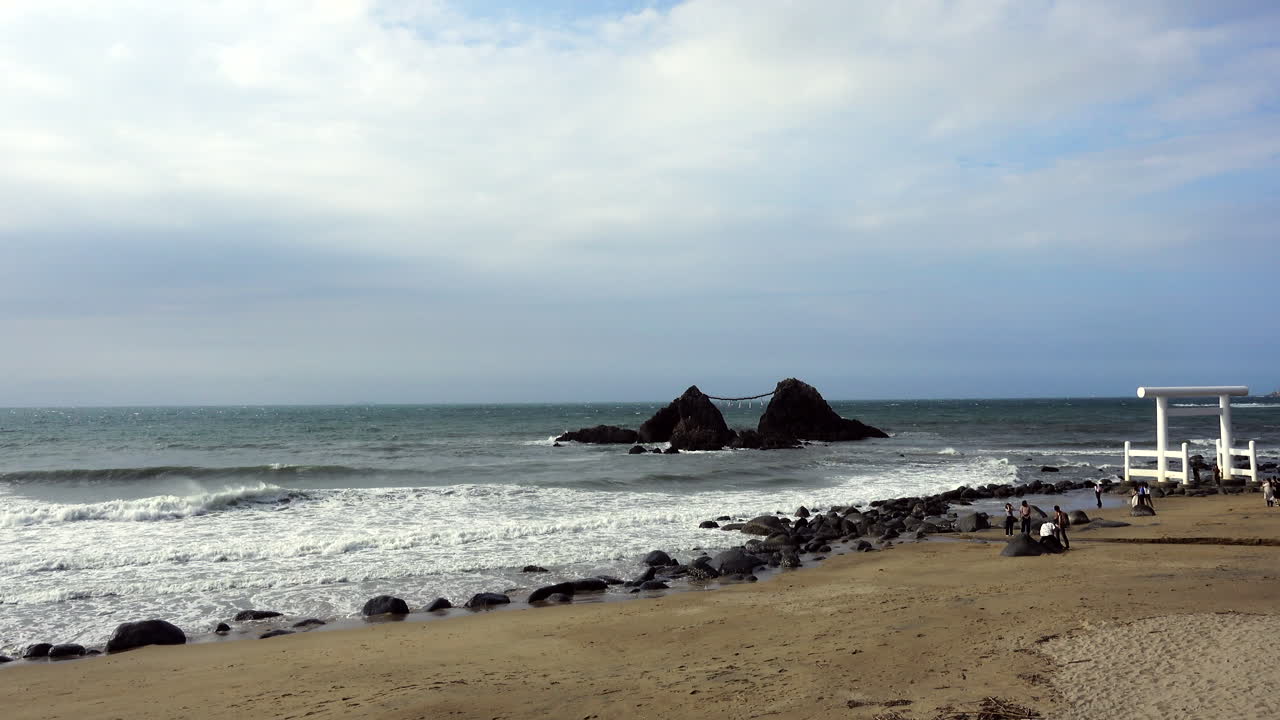 Marine waves reached the Fukuoka Sea Shrine seen from the sand of the beach with rocks on a windy day