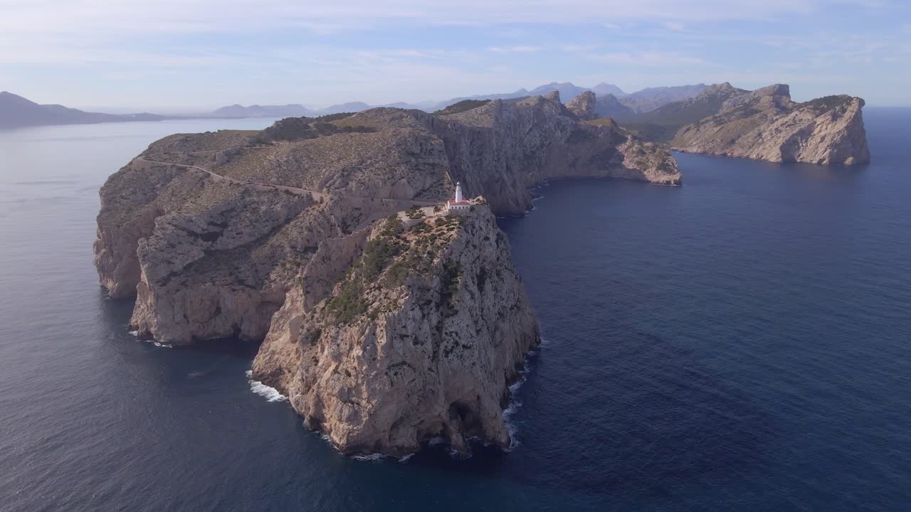 Stunning aerial perspective showcases the dramatic cliffs and clear blue waters surrounding the Faro de Formentor lighthouse in Mallorca. Experience the beauty of this spectacular coastal landscape.