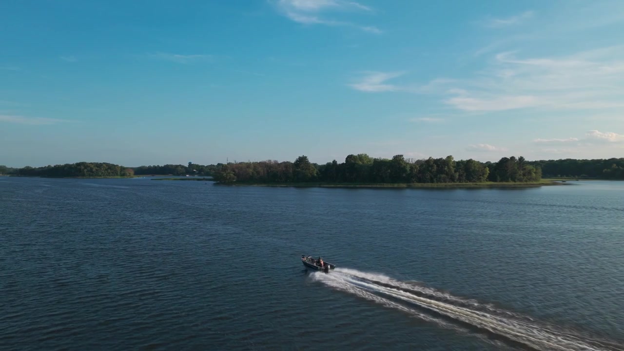 Wide aerial shot following a fishing boat on lake in upstate Minnesota during summertime. 4K