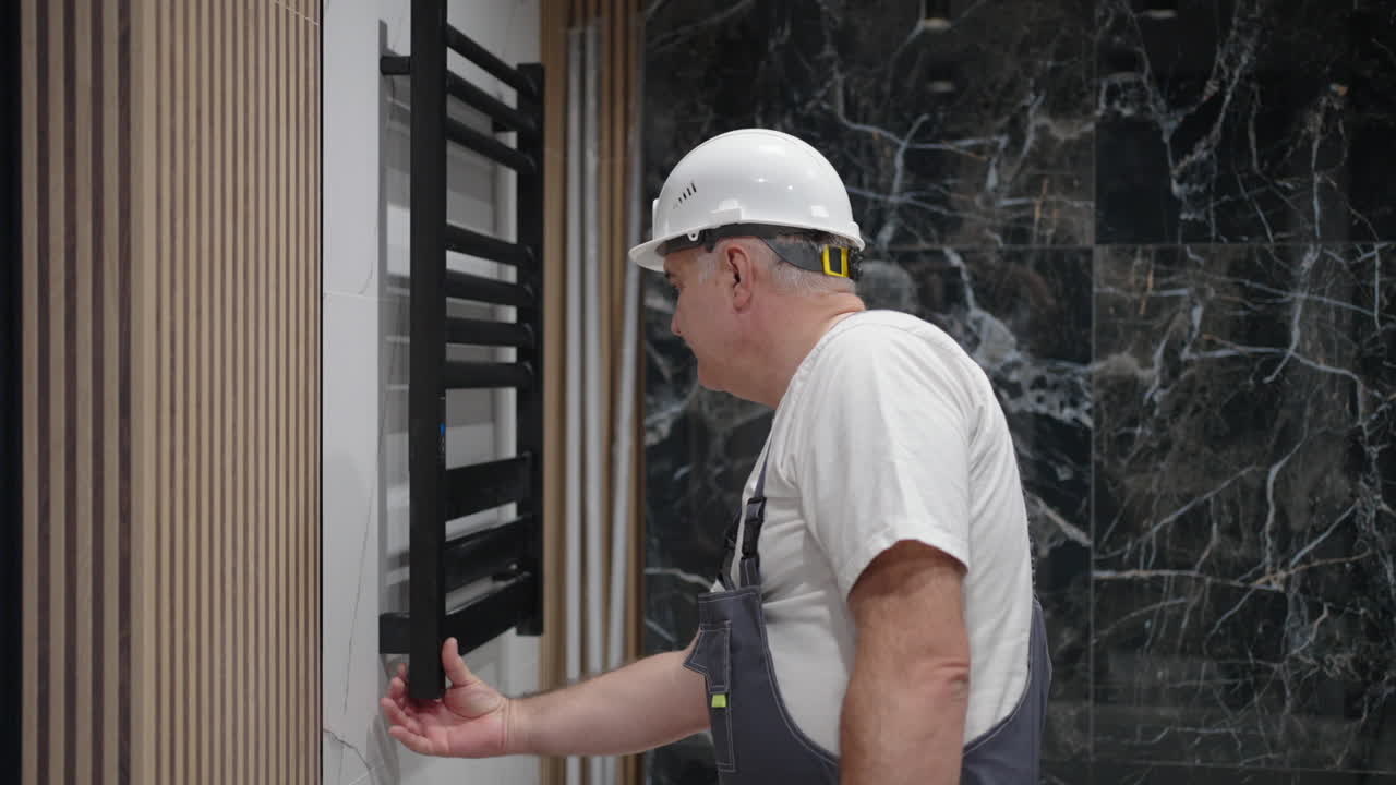 The plumber checks and turns on the heated towel rail to check the work in the bath.