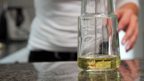 Close-Up-Of-Person-Pouring-Clear-Oil-In-Transparent-Glass-Container-Forming-Bubbles