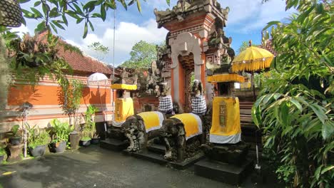 sacred temple gate in bali featuring traditional stone carvings, elephant statues, and yellow fabric-covered shrines, surrounded by tropical plants and vibrant architecture under clear sky