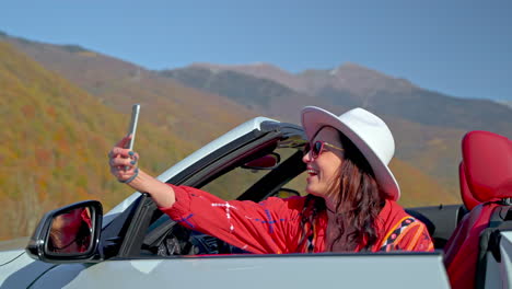 woman taking selfie in convertible car with mountain view