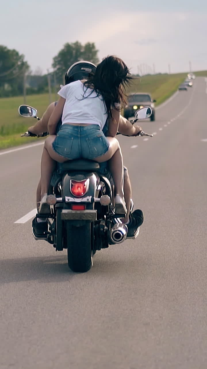 wonderful couple rides modern black motorbike between green trees and meadows against cars slow motion