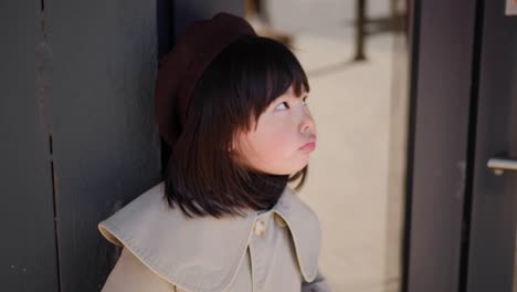 korean girl in a gray coat and cap stands the street in spring at the glass doors of the store