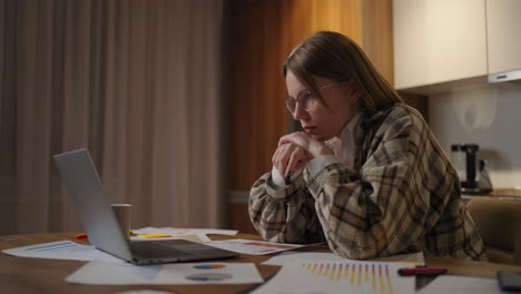 una mujer enfocada con gafas trabajando en documentos financieros sentada en el lugar de trabajo usando una aplicación de computadora portátil parece enfocada completando una tarea preparando la verificación de un informe.