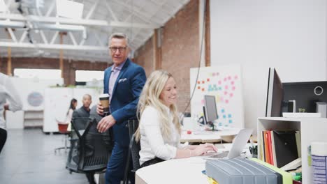 mature businessman talking to colleagues as they work at desks in modern open plan office