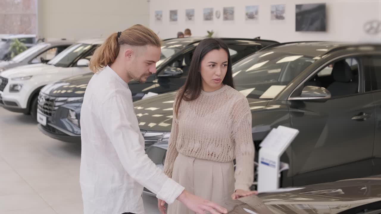 una hermosa pareja de jóvenes en la sala de exposición de automóviles eligiendo un coche nuevo para comprar.