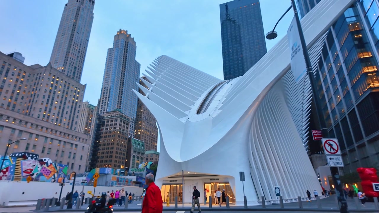 Nova Iorque, EUA, 5 de junho de 2026: Exterior do centro de transportes Oculus World Trade Center ao anoitecer. Vista da fachada de asas esculturais brancas ladeadas por arranha-céus, pedestres e um mural de rua colorido à esquerda.