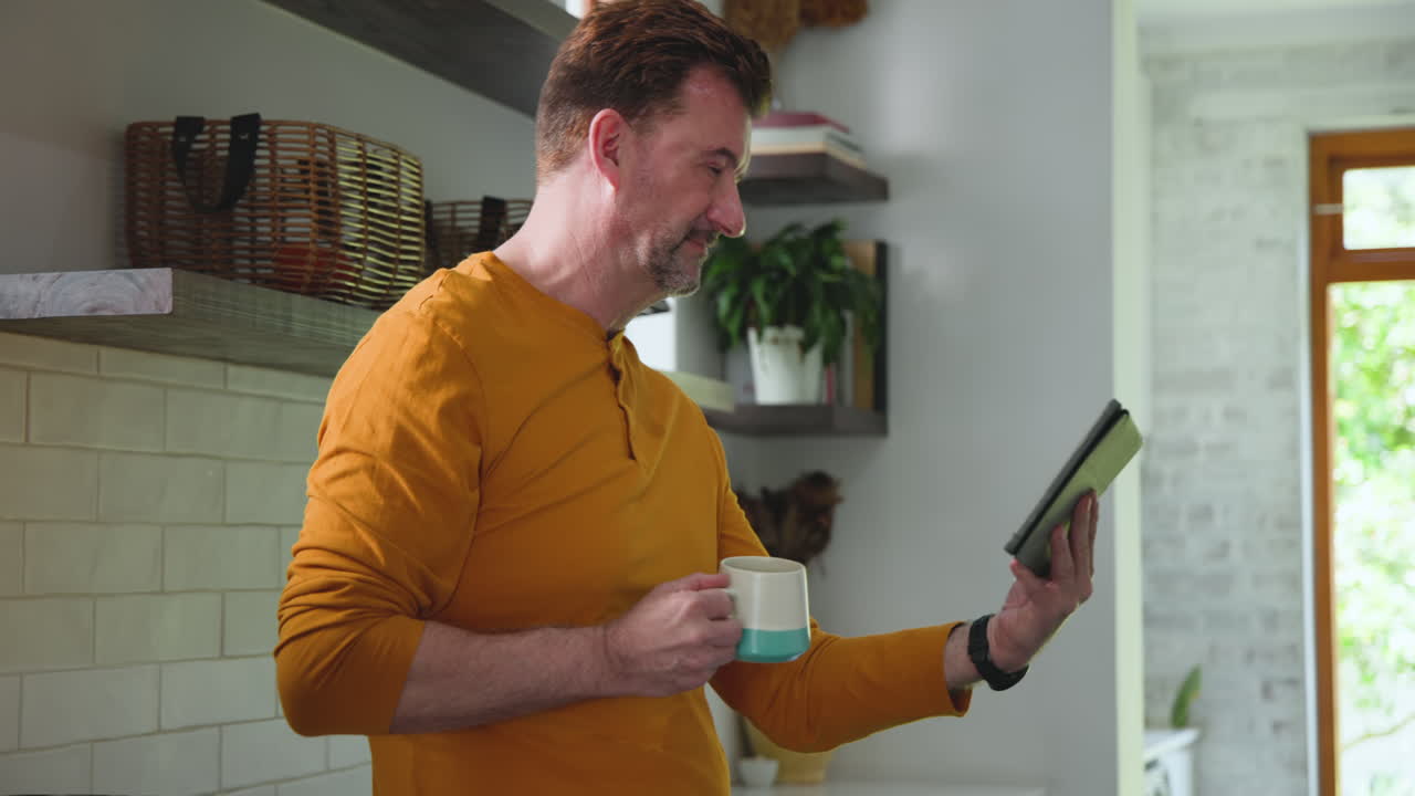 Smiling man holding tablet and coffee mug at home during video call