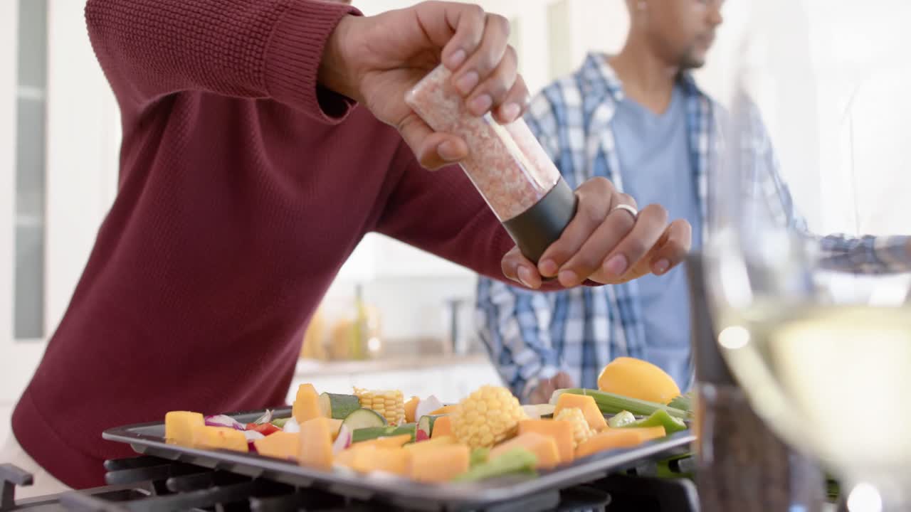 una feliz pareja afroamericana gay preparando la cena, aderezando verduras, cámara lenta