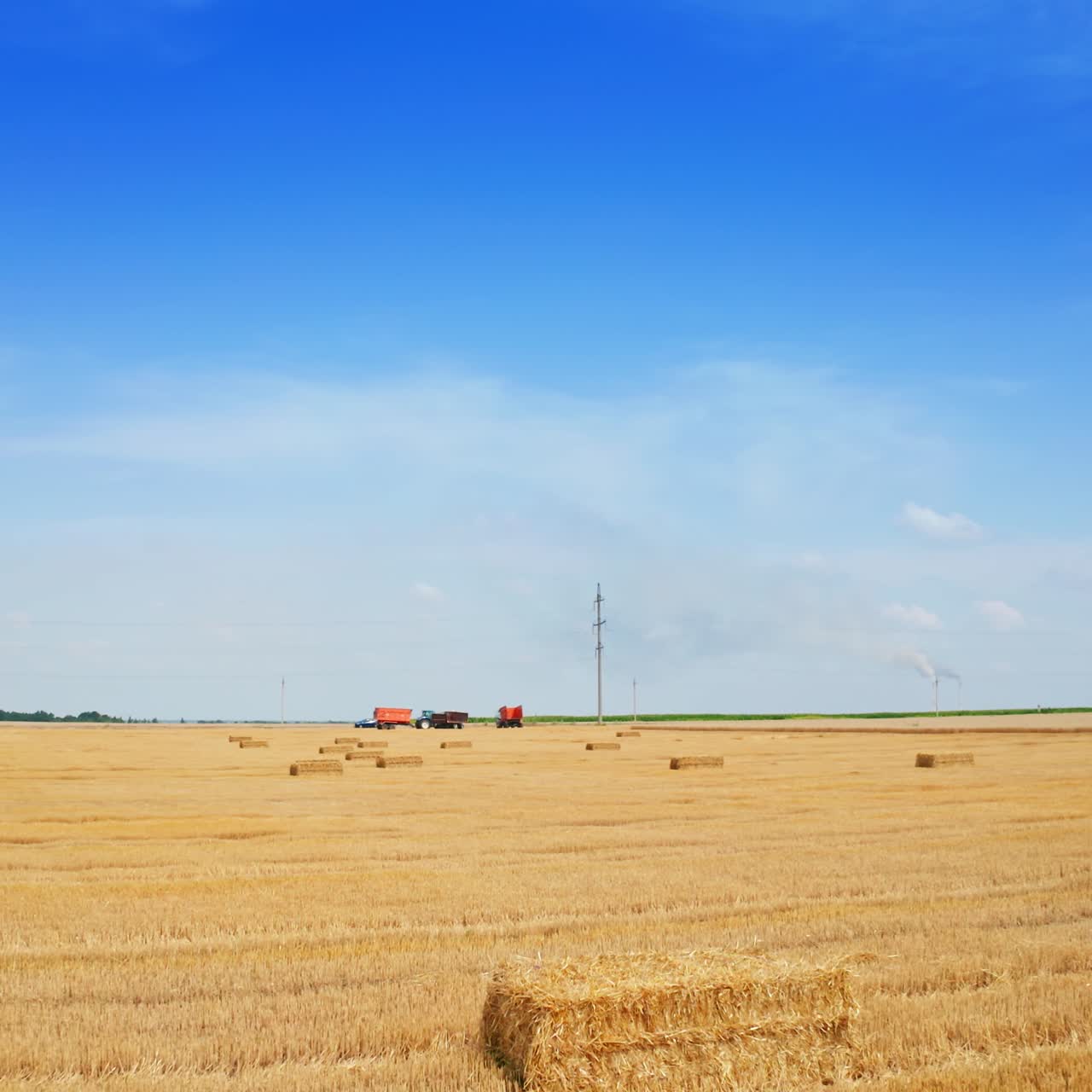 Contrasting blue sky with yellow field of mowed wheat and hay bales on. Fast approaching to the agricultural machinery standing in the field