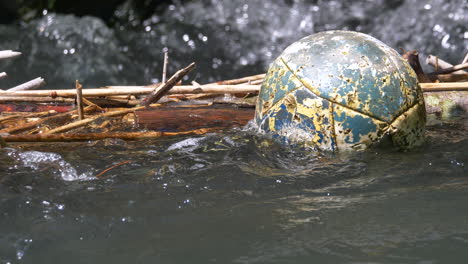 close up of old swimming ball in water in front of splashing waterfall in background, 4k prores shot